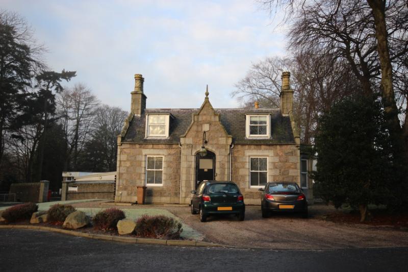 West Lodge, principal elevation, looking northwest, during daytime, on clear day, with parked cars in front of the building. 