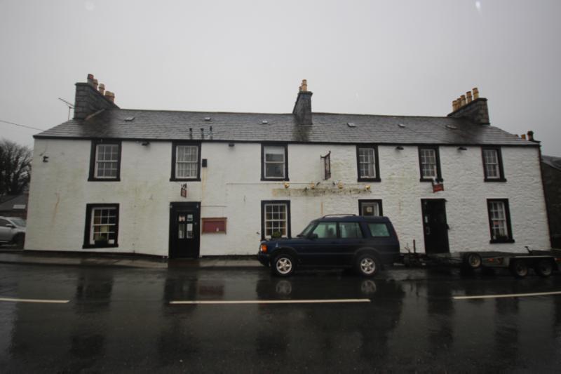 11 and 13 Main Street, Auchencairn, principal elevation, during daytime on a wet day with grey sky, with black painted window and door openings.