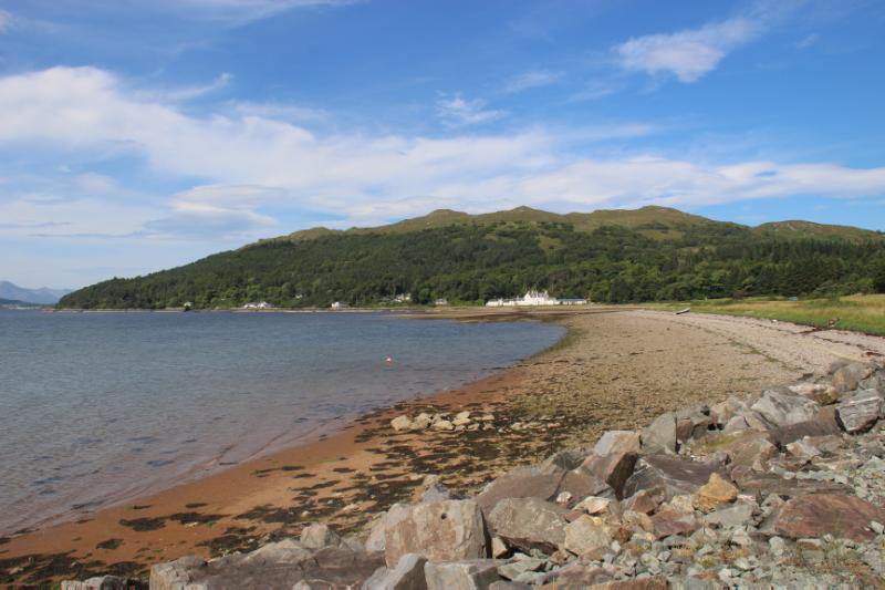 Distant view of Balmacara House (centre white house) and Lochalsh Woodland Garden from the east, on a clear day with blue sky. 