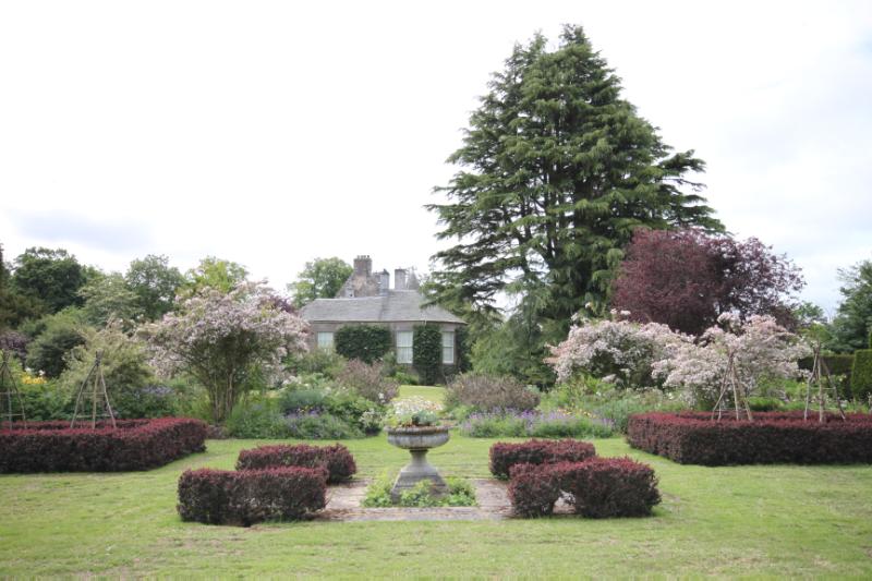 Walled garden looking southwest towards house and Atlas cedar, during daytime, on a clear day with white clouds in the sky. 