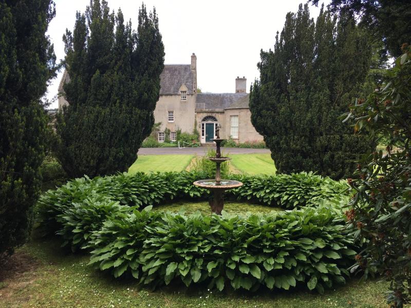 Water fountain and Irish Yews, looking west towards Malleny House, during daytime, on a cloudy day.