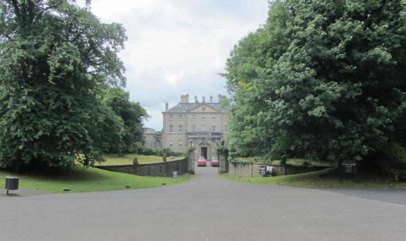 North front of Pollok House and entrance gate, during daytime, trees to left and right. 