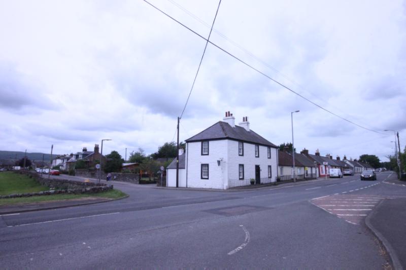 Corner House, looking west and showing the building in its village setting during daytime on a cloudy day.