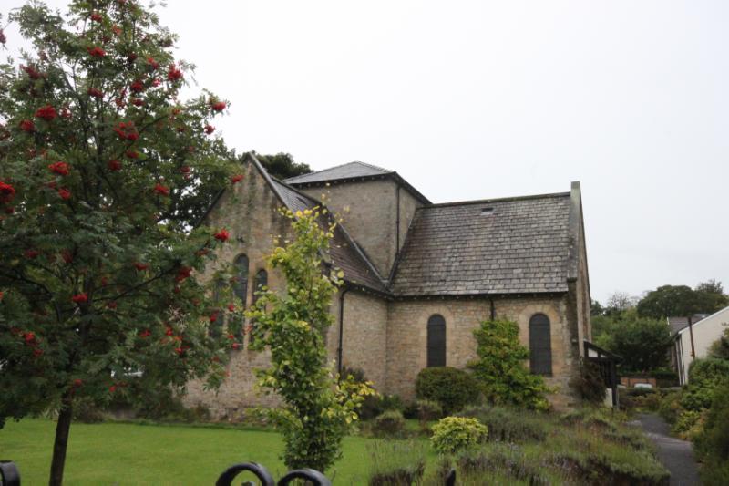 Church of the Holy Cross, looking south towards the north elevation, during daytime with trees and bushes in front of the church