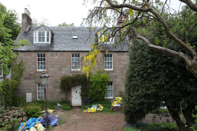 Bath Lodge, principal (south) elevation, looking north with a large tree in right foreground obstructing view of greenhouse. Taken during daytime on a cloudy day.