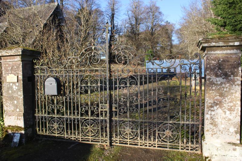 Close-up of iron gates and gatepiers with letterbox attached, looking northwest, during daytime with blue sky.