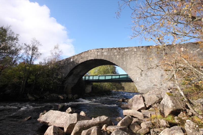 View of southeast elevation of Tummel military road bridge with replacement road bridge in background, with blue sky. 