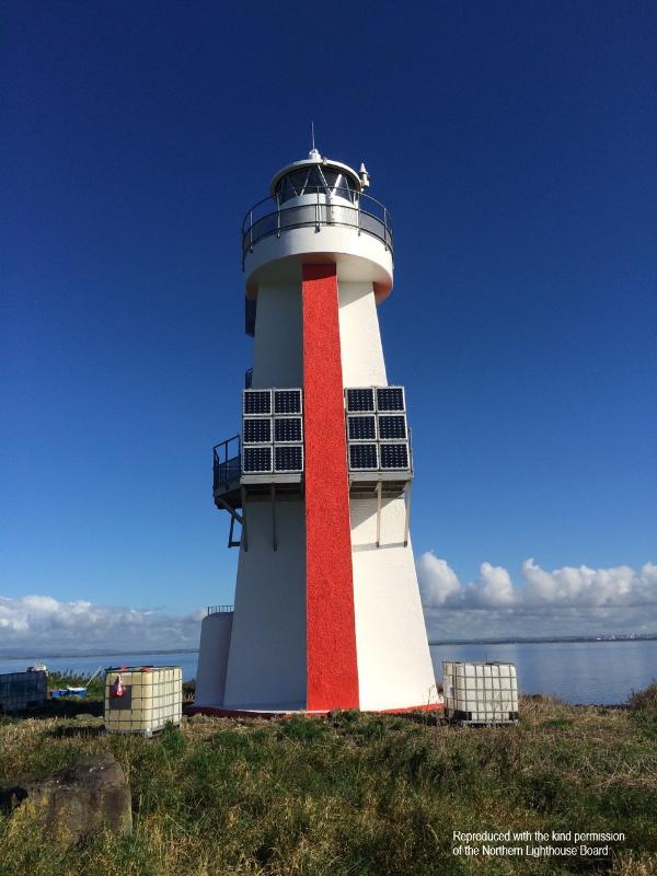 Lady Isle Lighthouse, showing the lighthouse tower, lantern, and solar panels on a sunny day, with views over towards the mainland. 