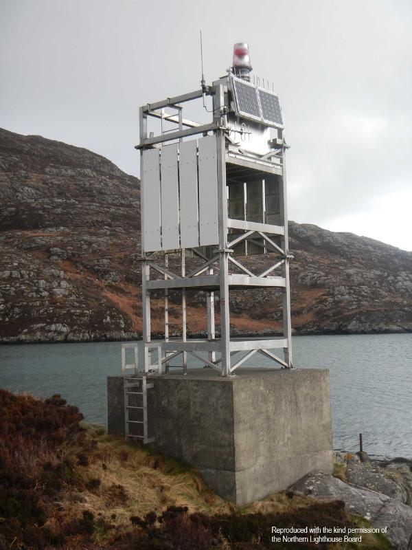 Calvay Lighthouse, South Uist, a solar-powered minor light, on a concrete base. Photograph taken on a cloudy day, with the sea and rocky hillside in the background. 