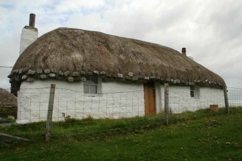 Glaic Cottage, southwest elevation, looking northeast, looking northeast, during daytime, with a wire fence infront of the building. 