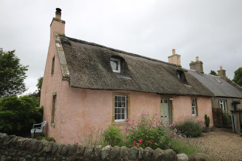 West End, Collessie entrance elevation looking north, during daytime with flowers and a rubble wall infront of the cottage.