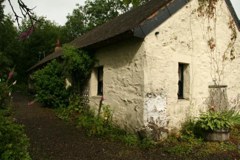 Weavers Cottage, south elevation of thatched cottage with bushes and flowers around the building. 