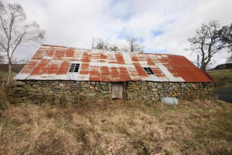 Cruck-frame Barn at Dounie, showing rubble west wall and corrugated roof, with trees in background, during daytime