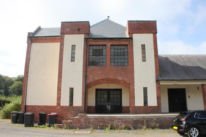 Former Creamery building, principal elevation, looking west, during daytime, on a sunny day with blue sky and clouds. 