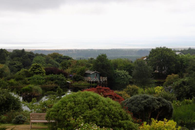 Glenwhan Gardens and Arboretum, looking from above in a southerly direction, over Glenwhan Lochan, with colourful planting in the foreground, and towards the coast at Luce Bay, on a cloudy day. 