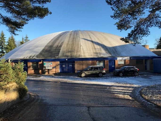 Bell’s Sports Centre, site entrance (west) elevation, looking east, during daytime, on clear day with blue sky. 