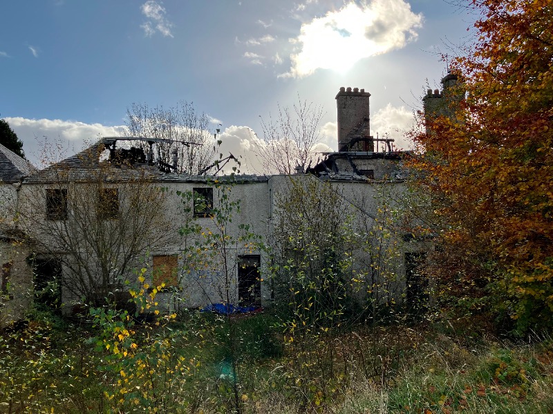 Former Rescobie Hotel, north elevation, looking south, with fire-damaged roof and some boarded window openings, during daytime, on cloudy day with intermittent blue sky.